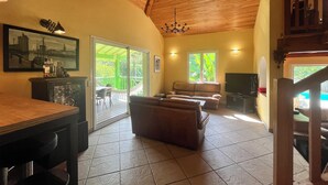 A spacious living room with a wooden ceiling, a large window, a sofa, a TV, and a dining area. - In the countryside near the beach (Saint-Barthelemy)