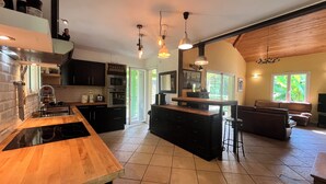 A modern kitchen with a central island, built-in oven, and a dining area with a bar stool. - In the countryside near the beach (Saint-Barthelemy)