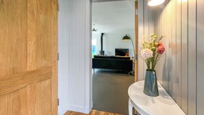 Ein Flur mit Holzboden, einer weißen Tür und einem weißen Konsolentisch mit Blumen in einer Vase.