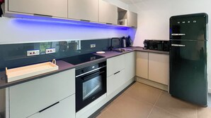 Eine moderne Küche mit Einbauofen, einem schwarzen Kühlschrank und einer blau beleuchteten Arbeitsfläche.