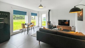 Ein modernes Wohnzimmer mit Sofa, Fernseher, Kamin, Esstisch und großen Fenstern.