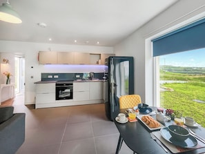 A modern kitchen with a dining area, a large window with a view of the countryside, and a table set for breakfast. - 1 bedroom accommodation in Dunvegan<br /> (Dunvegan<br />)