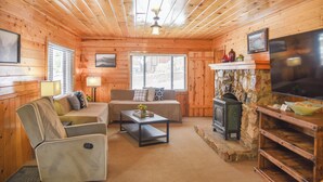 Ein gemütliches Blockhaus-Interieur mit Holzwänden, einem Steinkamin, einer Couch, einem Sessel und einem Fernseher.