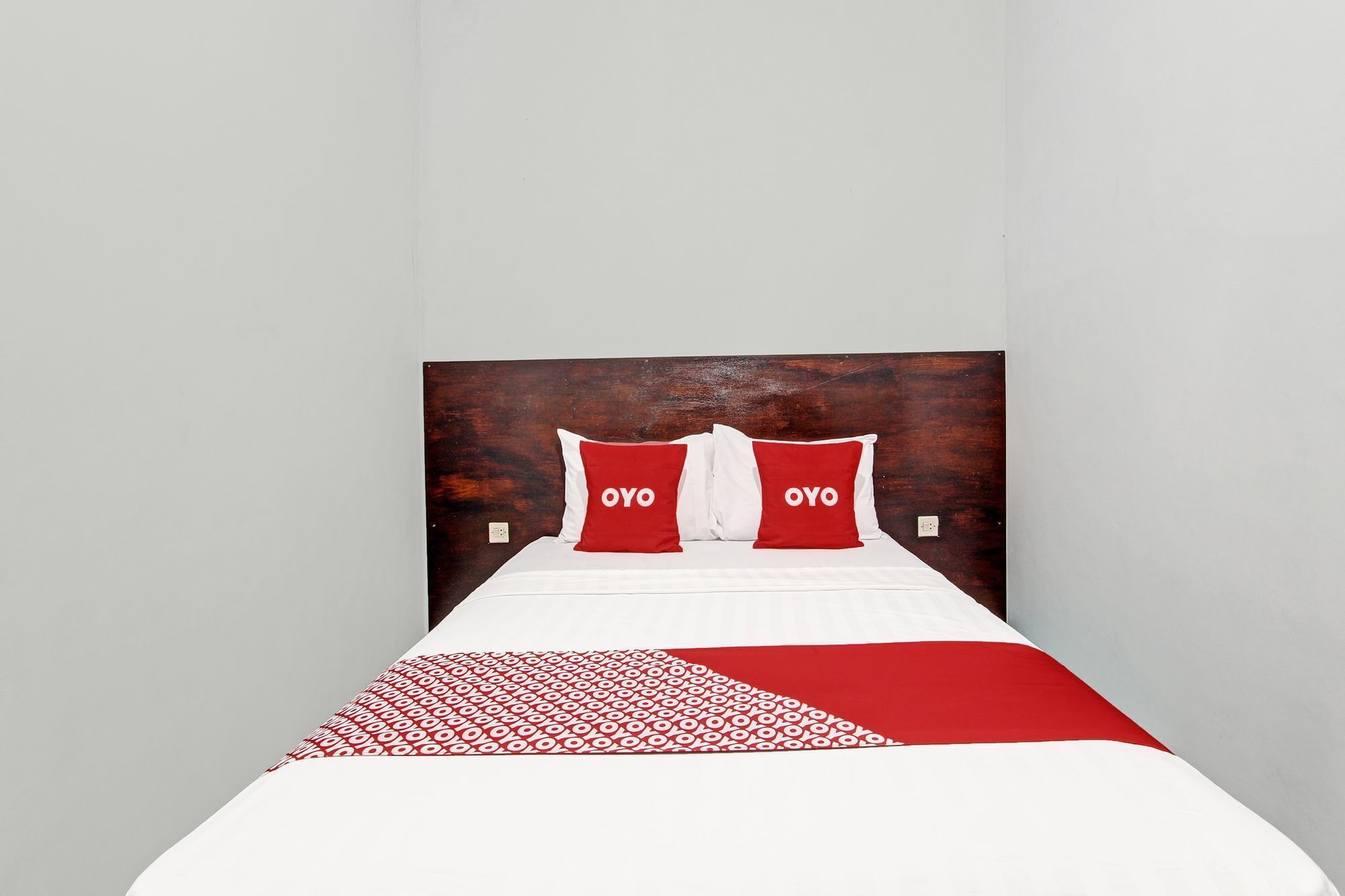 Ein Bett mit Holz-Kopfstütze, zwei Kissen mit dem Aufdruck "OYO" und einer gemusterten Bettdecke.