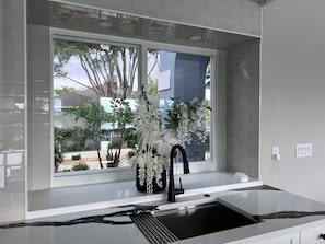 Eine moderne Küche mit großem Fenster, weißen Arbeitsplatten und einem schwarzen Wasserhahn.