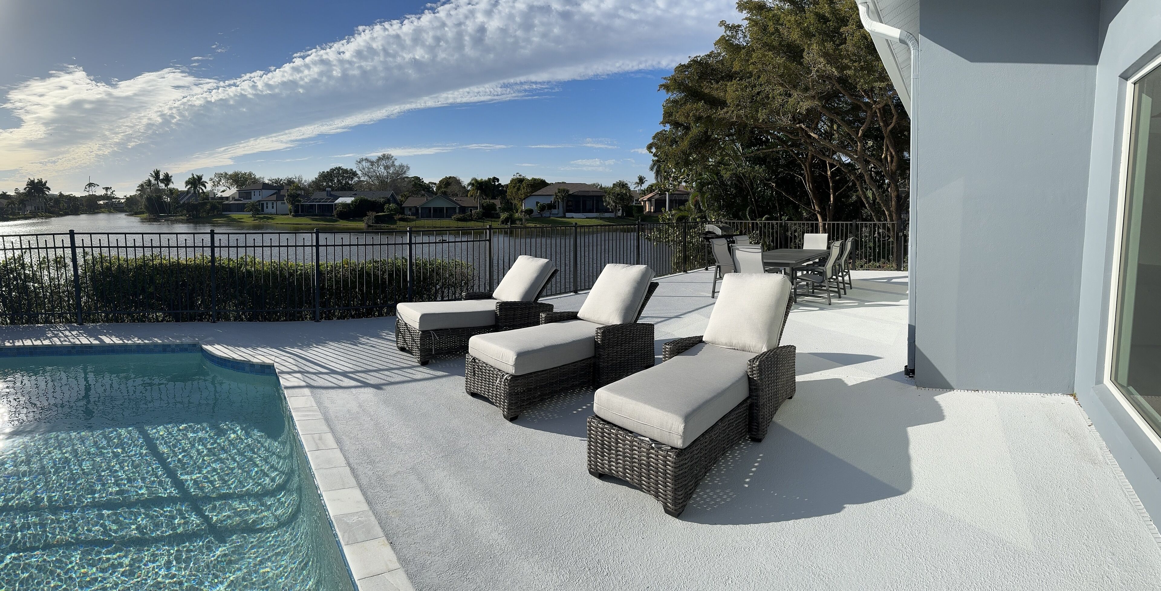 A poolside area with lounge chairs and a view of a lake and houses in the background.