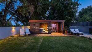A wooden cabin with a patio, two lounge chairs, a hot tub, and a small deck area.
