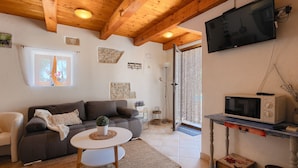 A cozy living room with a wooden ceiling, a grey sofa, a small round table, a television, and a microwave.