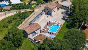An aerial view of a property with a swimming pool, lounge chairs, and a small building with a tiled roof.