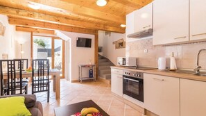 Une cuisine avec des poutres en bois, un coin repas avec des chaises, une table garnie de fruits et un escalier.