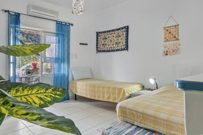 Quarto com duas camas, janela com cortinas azuis, um objeto decorativo na parede e um vaso com planta.