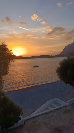 A sunset over a calm body of water with a boat, surrounded by natural landscape and a clear sky.
