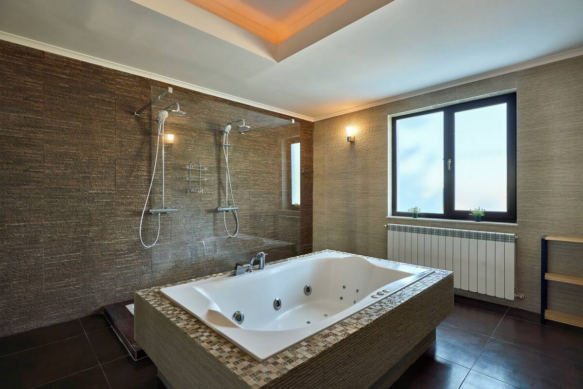 Une salle de bain moderne dotée d’une grande baignoire, d’un espace douche et d’une fenêtre laissant entrer la lumière naturelle.