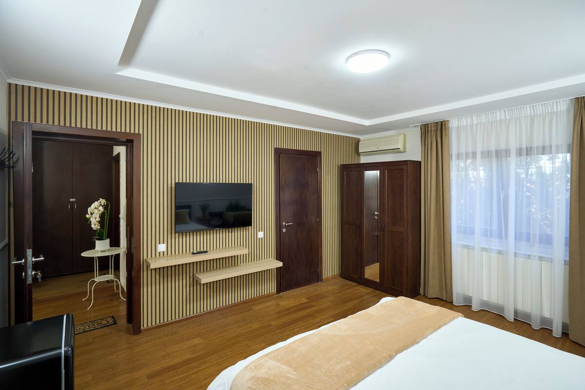 Une chambre d’hôtel avec un lit, un téléviseur fixé au mur, un lambris en bois, une armoire et une fenêtre avec des rideaux.