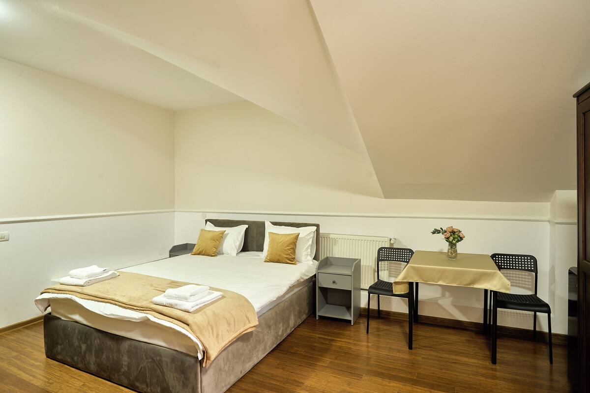 Une chambre à coucher comprenant un lit, une table de chevet, une chaise et une petite table sur laquelle est posé un vase.