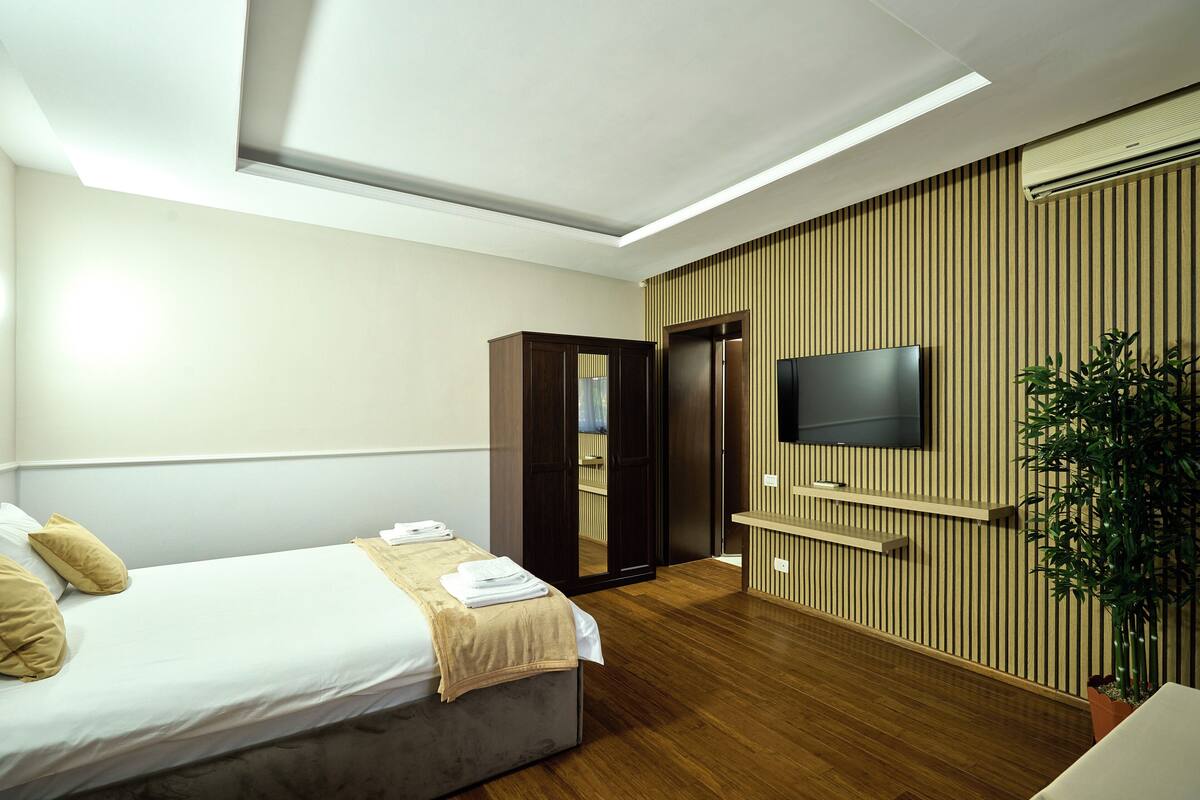 Une chambre d’hôtel moderne avec un lit, un téléviseur fixé au mur, un mur recouvert de panneaux en bois et une plante.
