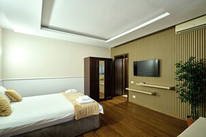 Una habitación de hotel moderna con cama, televisor montado en la pared, panel de pared de madera y una planta.