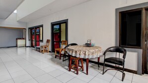 A spacious room with a tiled floor, a round table with a patterned tablecloth, and several wooden chairs. - Hotel O Kd House (Semarang)