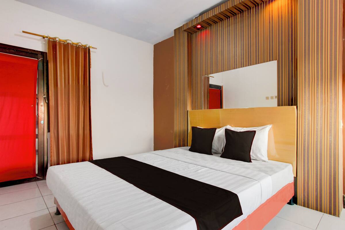 A hotel room with a large bed, a red door, and striped curtains.