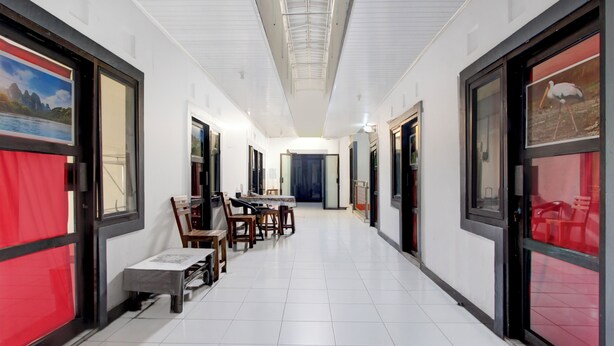 A hotel corridor with a dining area featuring a long table and chairs, large windows with artwork, and a tiled floor. - Hotel O Kd House (Semarang)