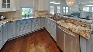 Una cocina con encimera de granito, muebles blancos y lavavajillas.