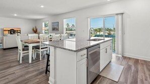 A modern kitchen with white cabinetry, a granite countertop, and a large window offering a view of the outdoors. - Turtle Paradisena | Spacious Home Just One Block From the Beach! (Daytona Beach)