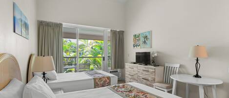 A hotel room with two beds, a TV, a desk, and a view of greenery.