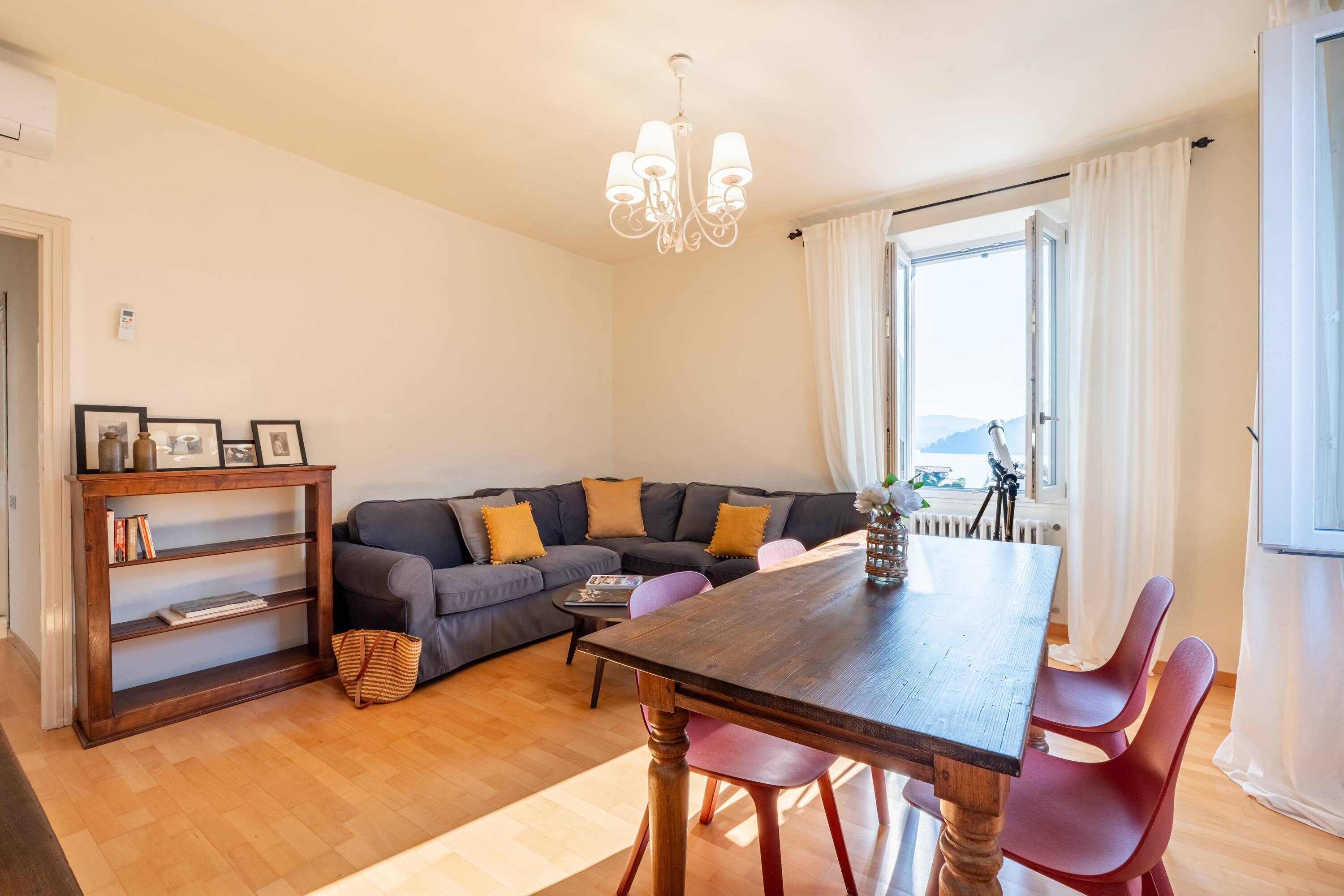 A living room with a wooden dining table, red chairs, a grey sofa, and a wooden bookshelf.