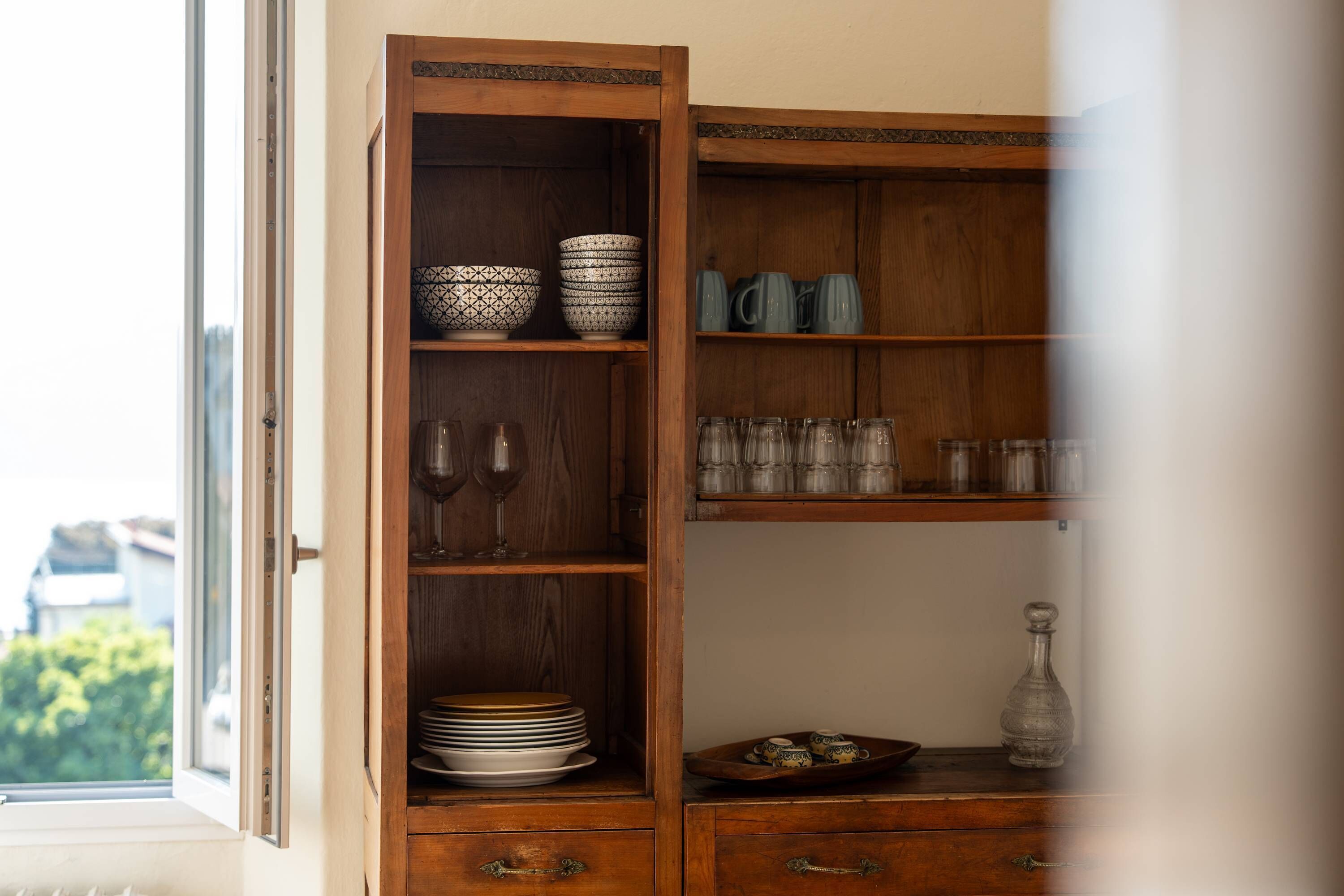 A wooden cabinet with shelves containing bowls, wine glasses, and plates.