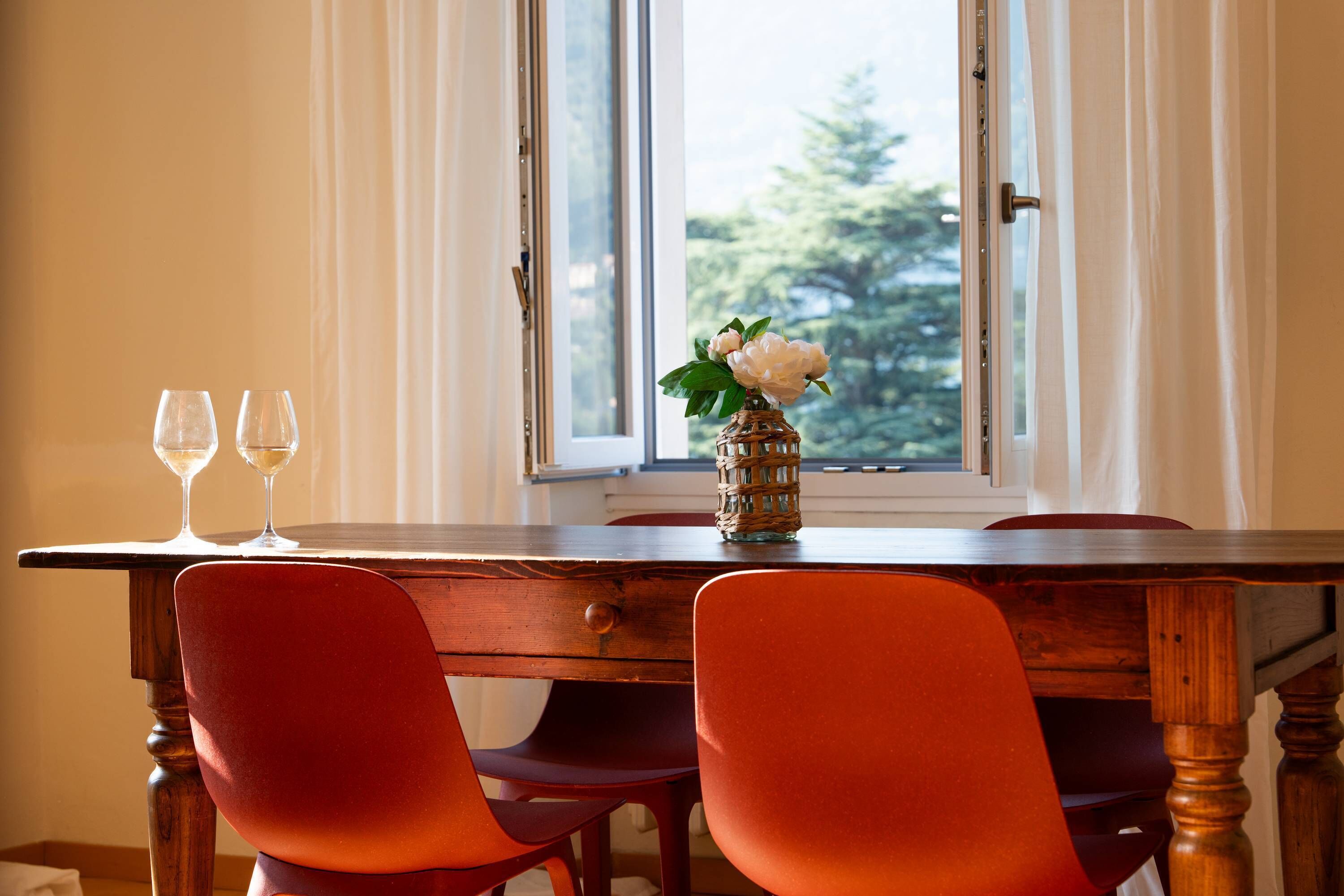 Une table à manger avec deux verres à vin et un vase de fleurs, le tout placé devant une fenêtre ornée de rideaux.
