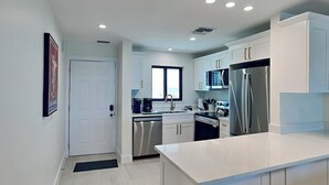 A modern kitchen with white cabinets, stainless steel appliances, and a large island. - Seaside 505 | Top-Floor w. Views +Amenities (Fort Myers Beach)