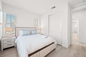 Un dormitorio con una cama grande, dos mesitas de noche con lámparas, un armario y una puerta que da a otra habitación.