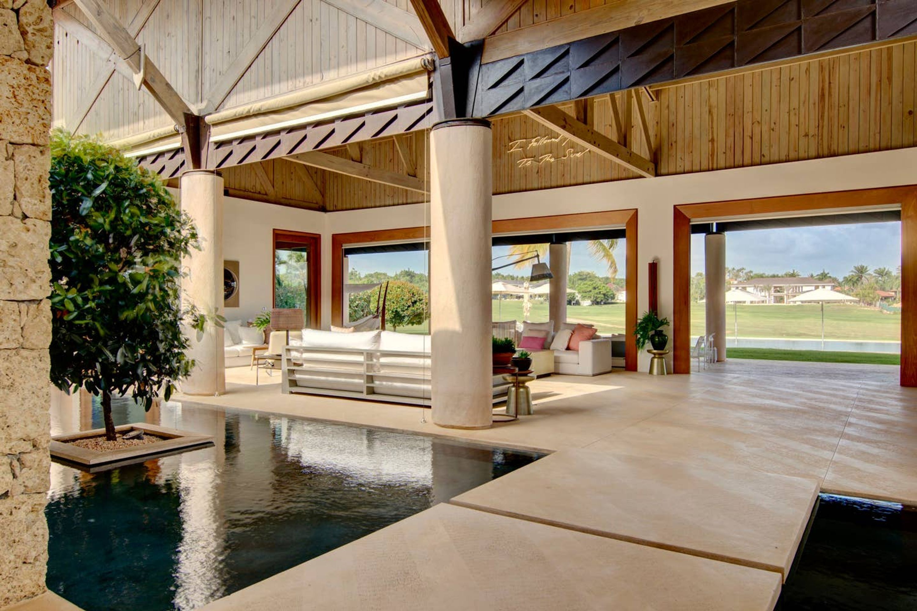A spacious indoor area with a large pool, wooden ceiling beams, and a view of a golf course.