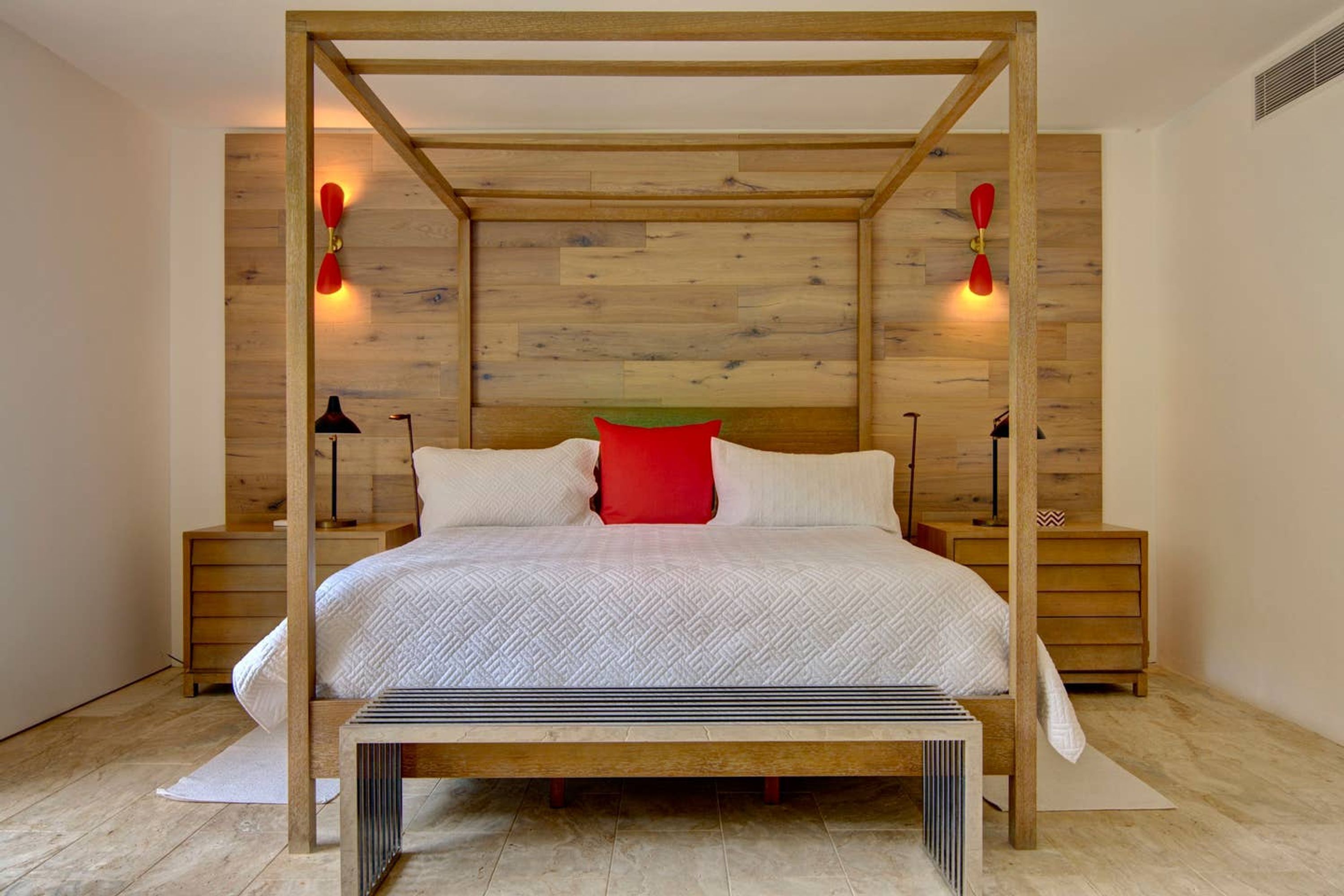 A bedroom with a wooden four-poster bed, white bedding, a red pillow, and two bedside tables with lamps.
