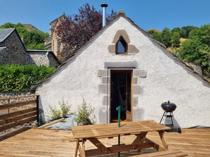 Un bâtiment rustique en pierre, avec un banc en bois et un barbecue devant.