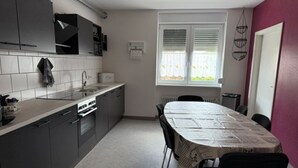 A compact kitchen with a dining table, a window with blinds, and a door. - Horizon 360° (Kitzingen)