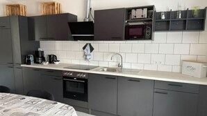 A modern kitchen with grey cabinets, a built-in microwave, a sink, and a stove. - Horizon 360° (Kitzingen)