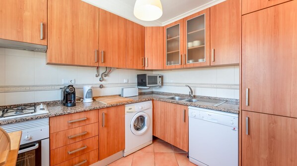 A compact kitchen with wooden cabinets, a microwave, a coffee maker, a washing machine, and a dishwasher.