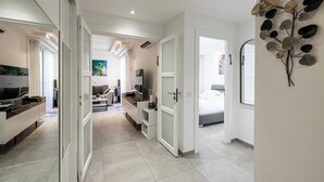Een moderne, goed verlichte kamer met een groot bed, een bureau en een zithoek. Er is een deur naar een andere kamer en een decoratie hangt aan de muur.