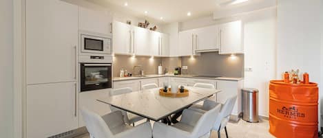 Une cuisine moderne avec des meubles blancs, un plan de travail en marbre et un coin repas comprenant une table et des chaises en verre.