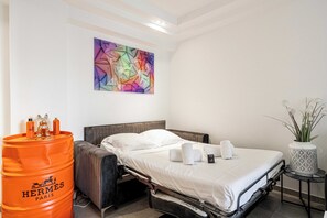 Ein Hotelzimmer mit einem Bett, einer großen orangefarbenen Tonne, einer dekorativen Vase und einem farbenfrohen abstrakten Gemälde an der Wand.
