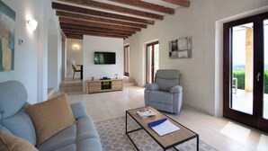 A spacious living room with a sofa, armchair, and coffee table. A television is mounted on the wall, and there is a staircase leading to another level. - Finca Lejania - Modern villa near Manacor with panoramic views (manacor)