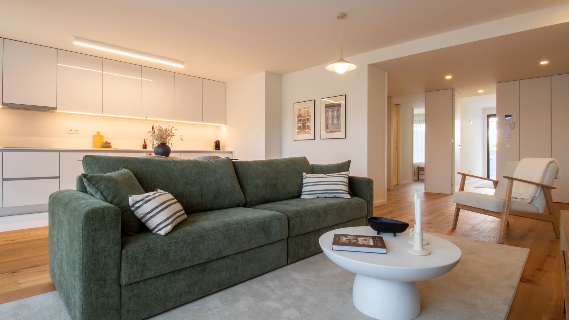 A modern living room with a green sofa, a white coffee table, and a kitchen in the background.