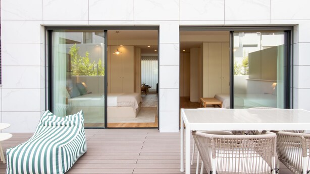 A modern hotel room with a sliding glass door leading to a balcony, a bed, a small table, and wicker furniture. - Gaia Elegant Apartment w/ Patio by LovelyStay (Vila Nova de Gaia)