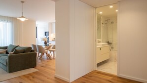 A modern living room with a sofa, chairs, and a glass dining table. There is a kitchen area in the background with a stove and cabinets. - Gaia Elegant Apartment w/ Patio by LovelyStay (Vila Nova de Gaia)