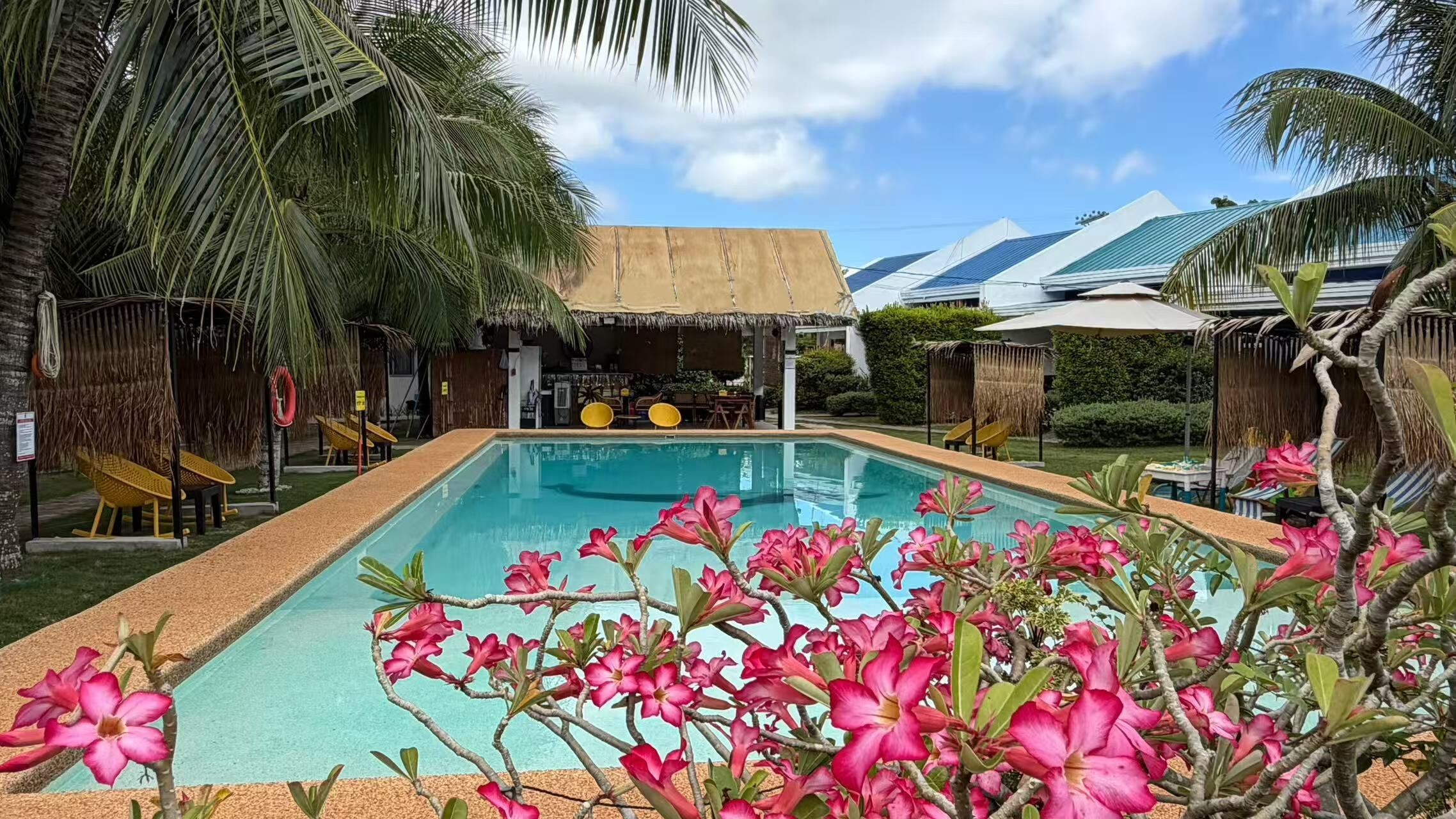 A swimming pool with a tropical garden, palm trees, and a thatched-roof structure.