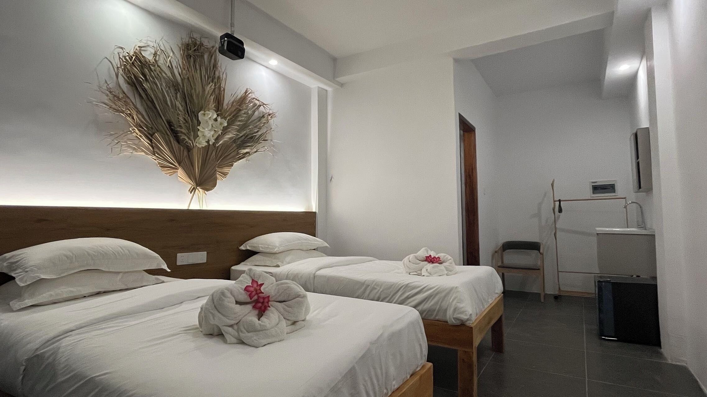 A hotel room with two beds, a wooden headboard, a wall-mounted light fixture, and a bathroom with a sink and mirror.