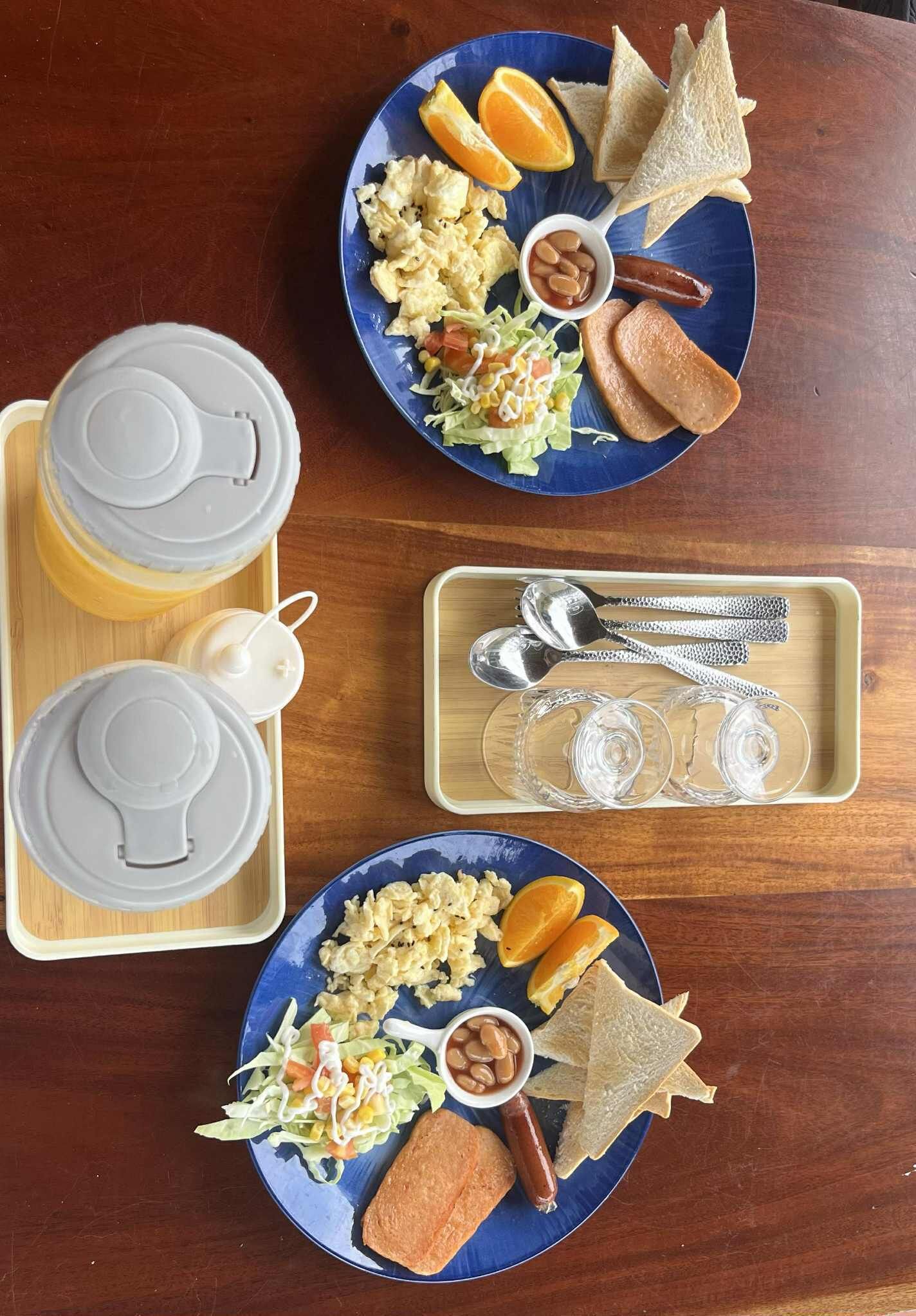 Two plates of breakfast food, including scrambled eggs, toast, and orange slices, on a wooden table.