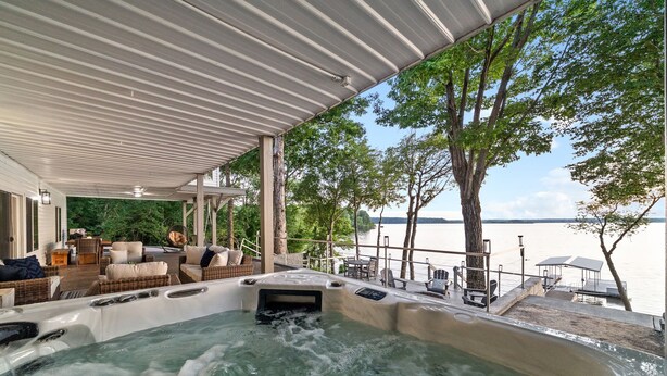 A hot tub area with a covered deck, outdoor furniture, and a view of the water. - Bluebird Sanctuary • Serene Sunset Escape (Big Sandy)