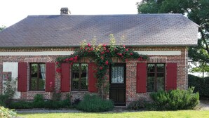 Un edificio de ladrillo con contraventanas rojas, una puerta negra y un arco de flores.